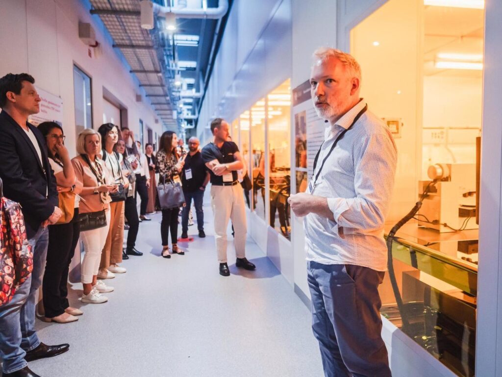 A line of people standing facing a series of PC2 laboratories and listening to the tour lead.